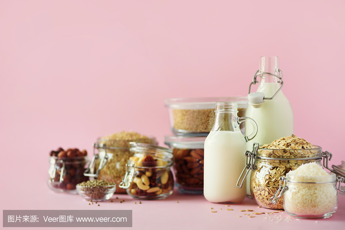 素食代替牛奶。玻璃瓶與非乳制品的牛奶和原料在粉紅色的背景與復制空間。清潔飲食,無乳制品,素食,防過敏,健康的食品理念